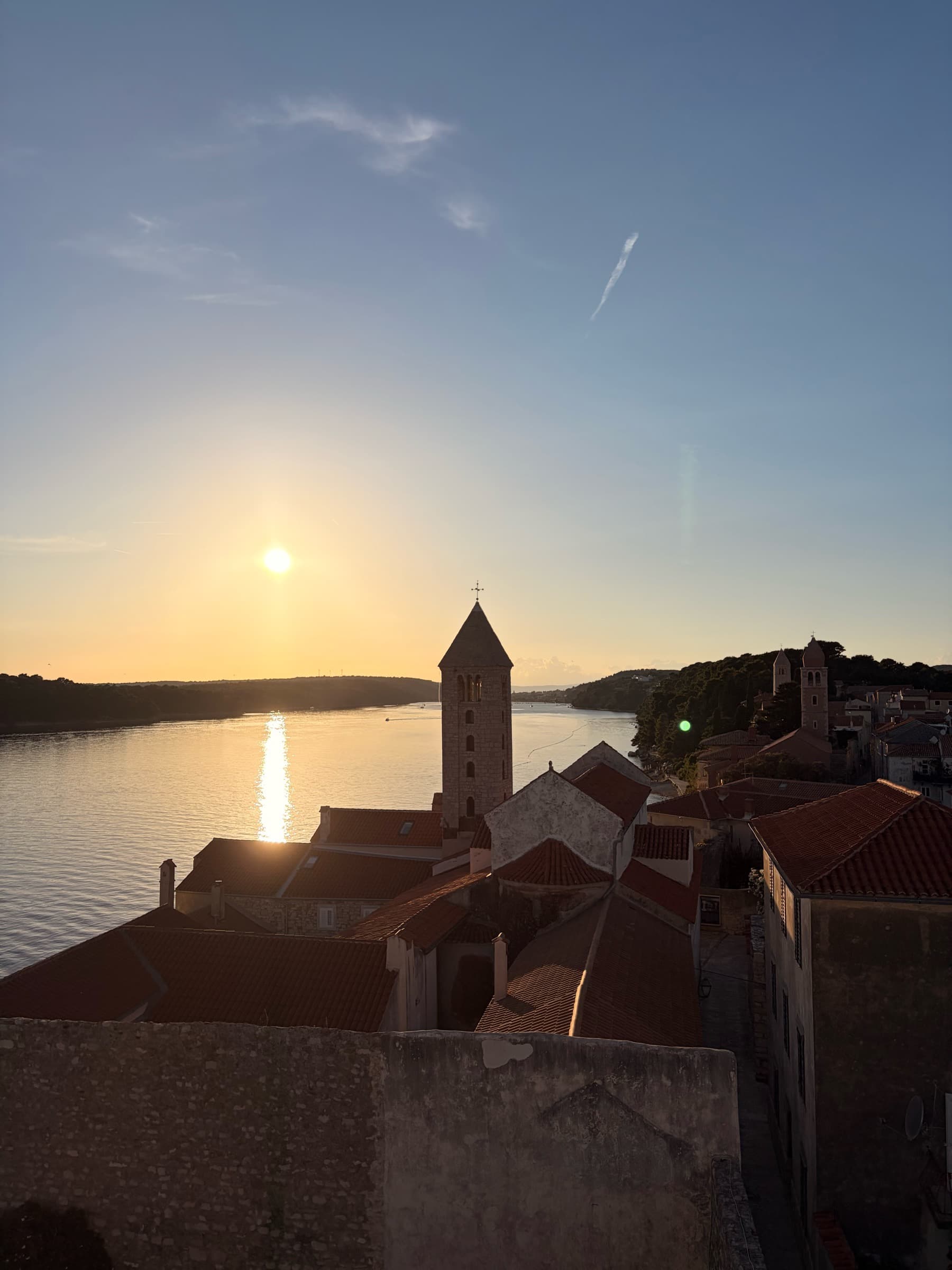 Red roofs of Rab's historic core and a bell tower in soft sunset light.