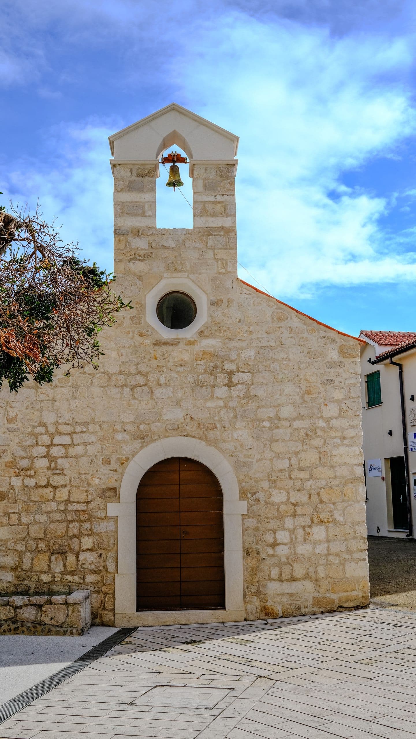 A small weathered stone church facade with a bell-cote, old town, clear day.