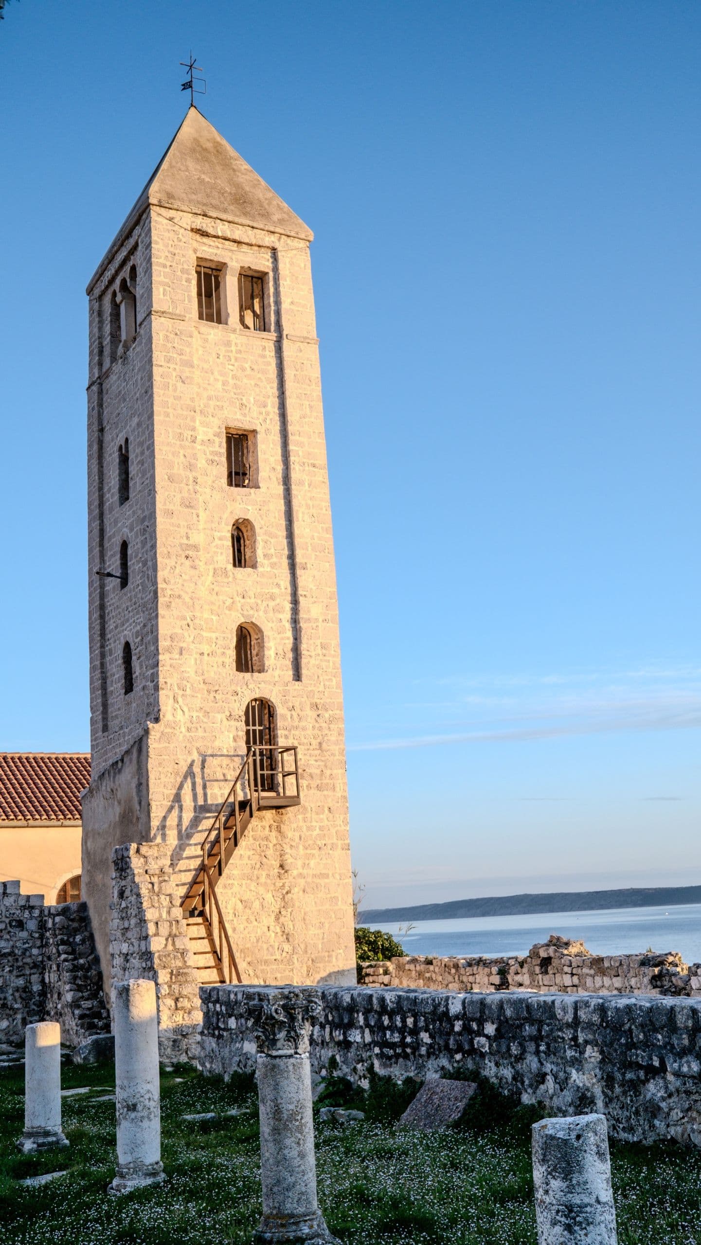 The Rab bell tower in warm low light, the sea beyond — six centuries of stone.