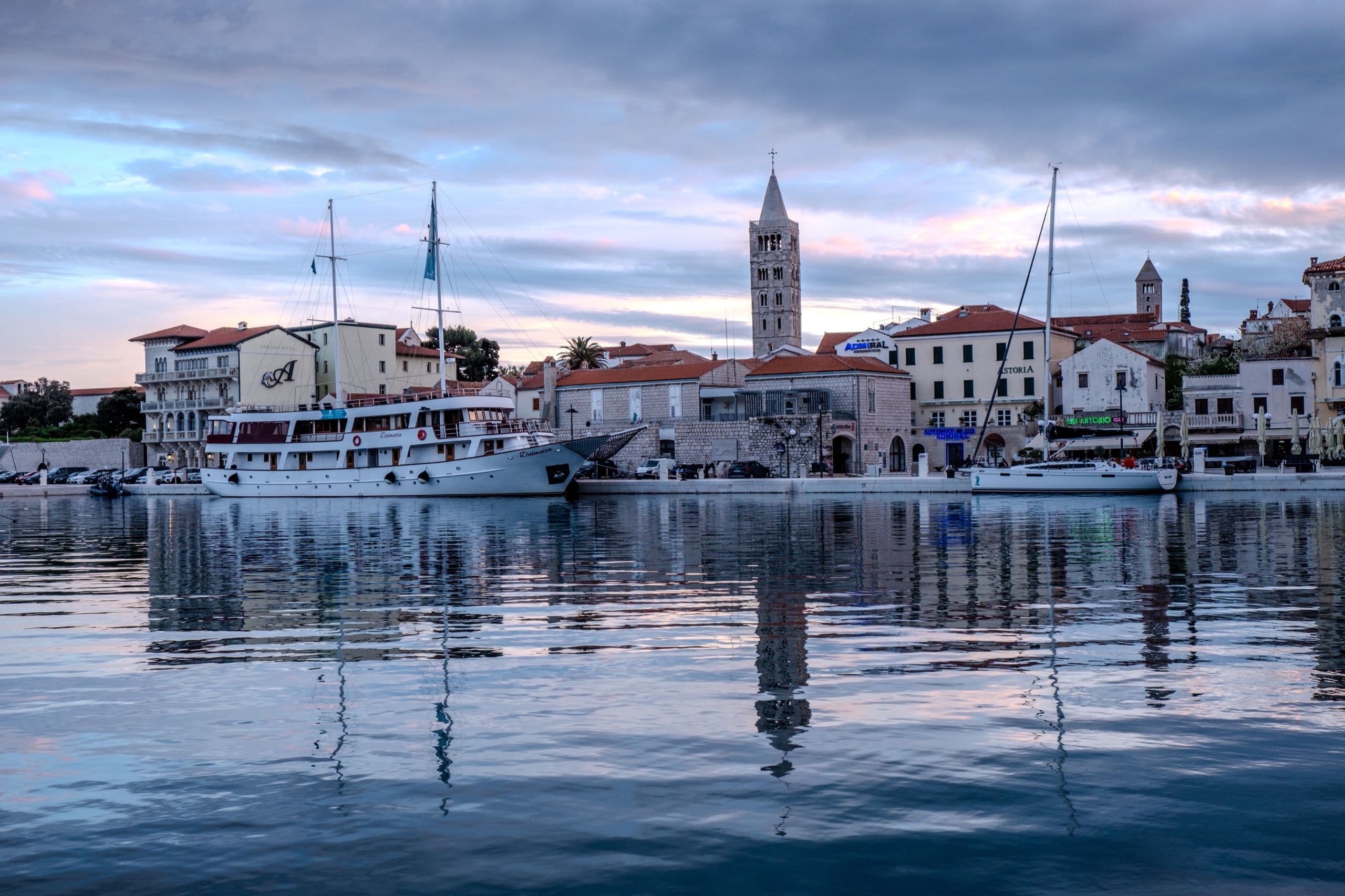 Rab old town and harbour seen across calm water.