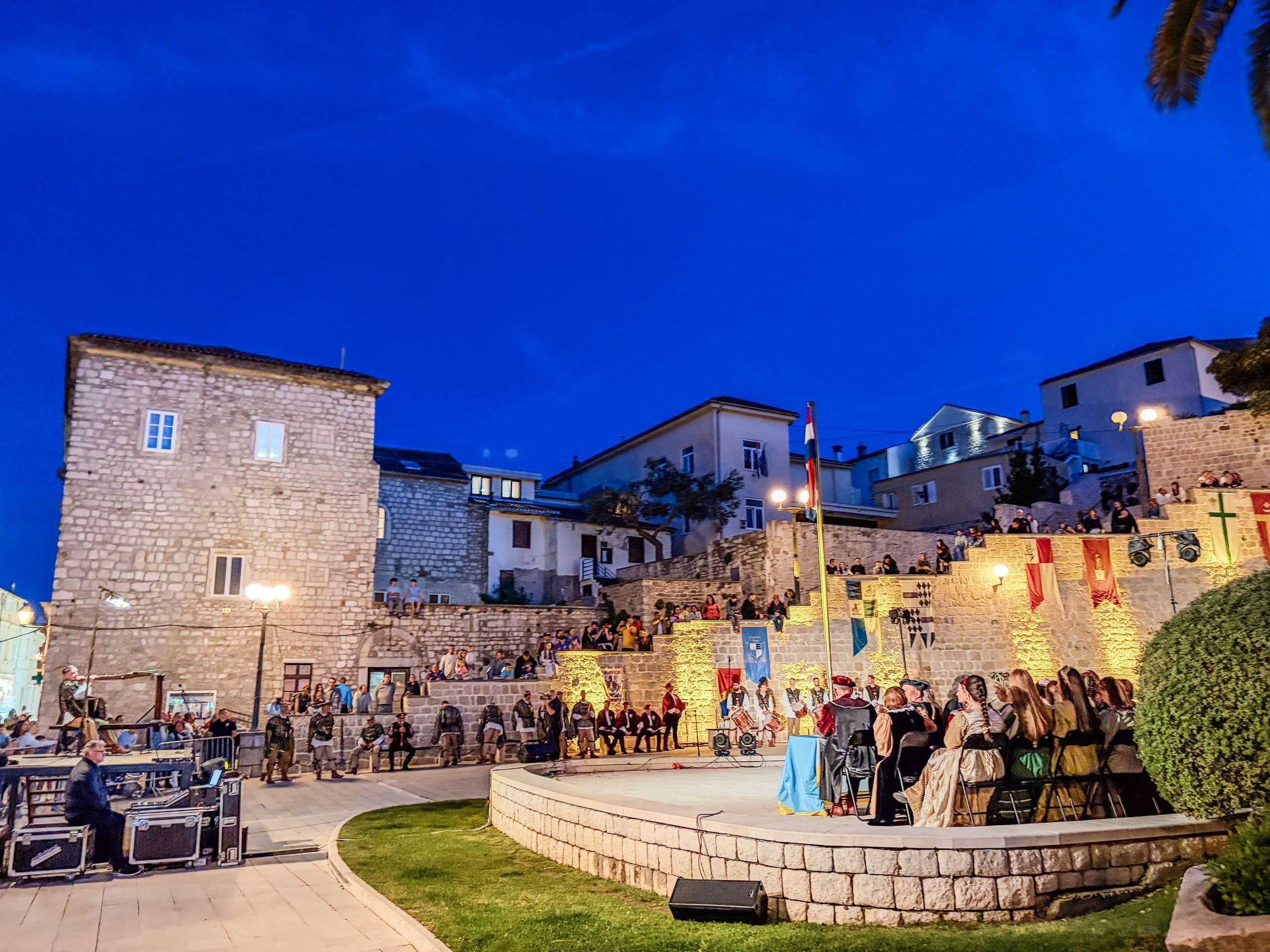 Festival night on a Rab old town street, warm lanterns and gathered crowd.