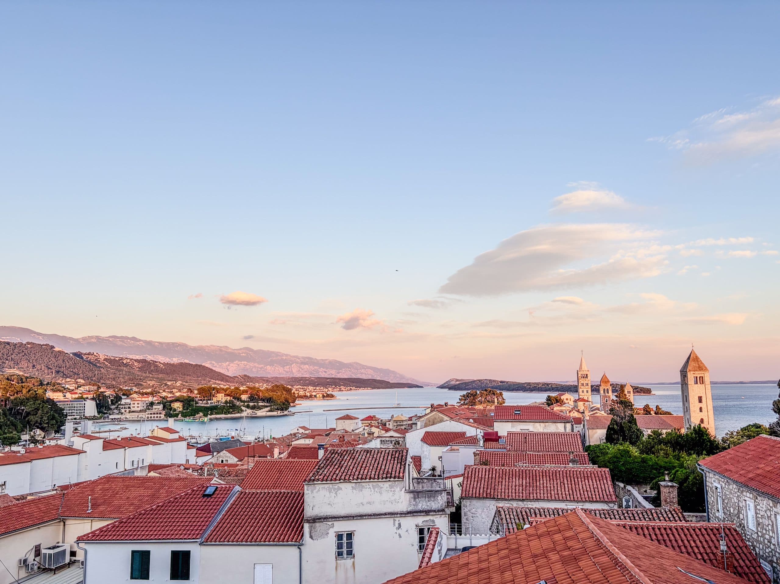 Panoramic Rab old town rooftops and bell towers at golden hour.