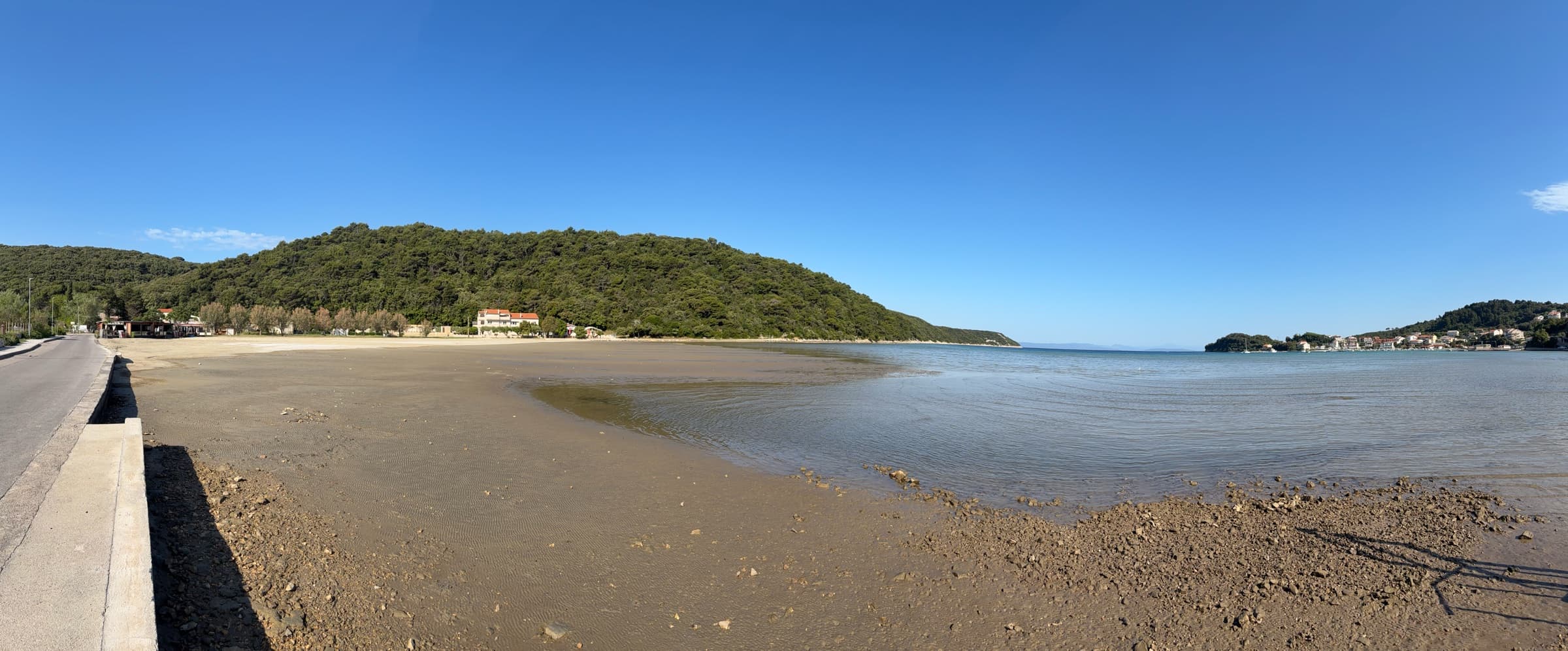 Wide view of shallow water, sandy Mel Beach and the wooded Kampor shoreline.
